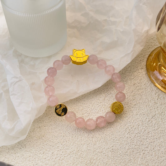 Rose quartz crystal bracelet with gold and black charms representing love and connection