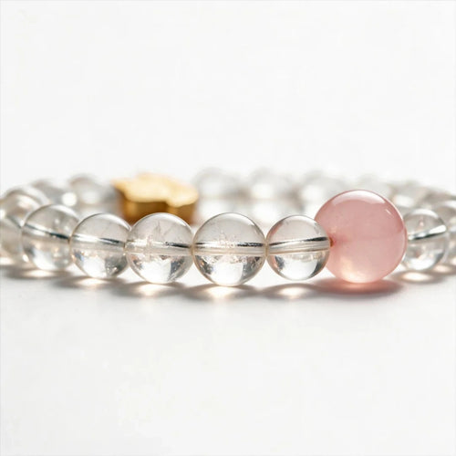 Orbii clear quartz crystal bead bracelet with a single pink accent bead and gold NFC charm on a white background.